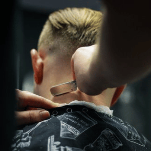 Barbeiro utilizando navalha para finalizar corte de cabelo no estilo fade.